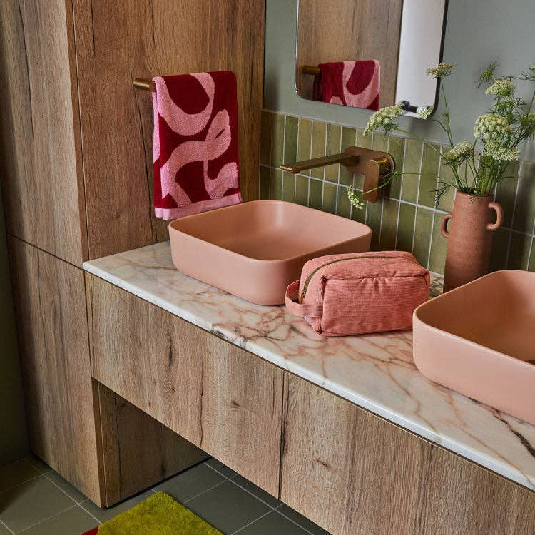 Bathroom with pink sinks, towel, and toiletries on a marble countertop.