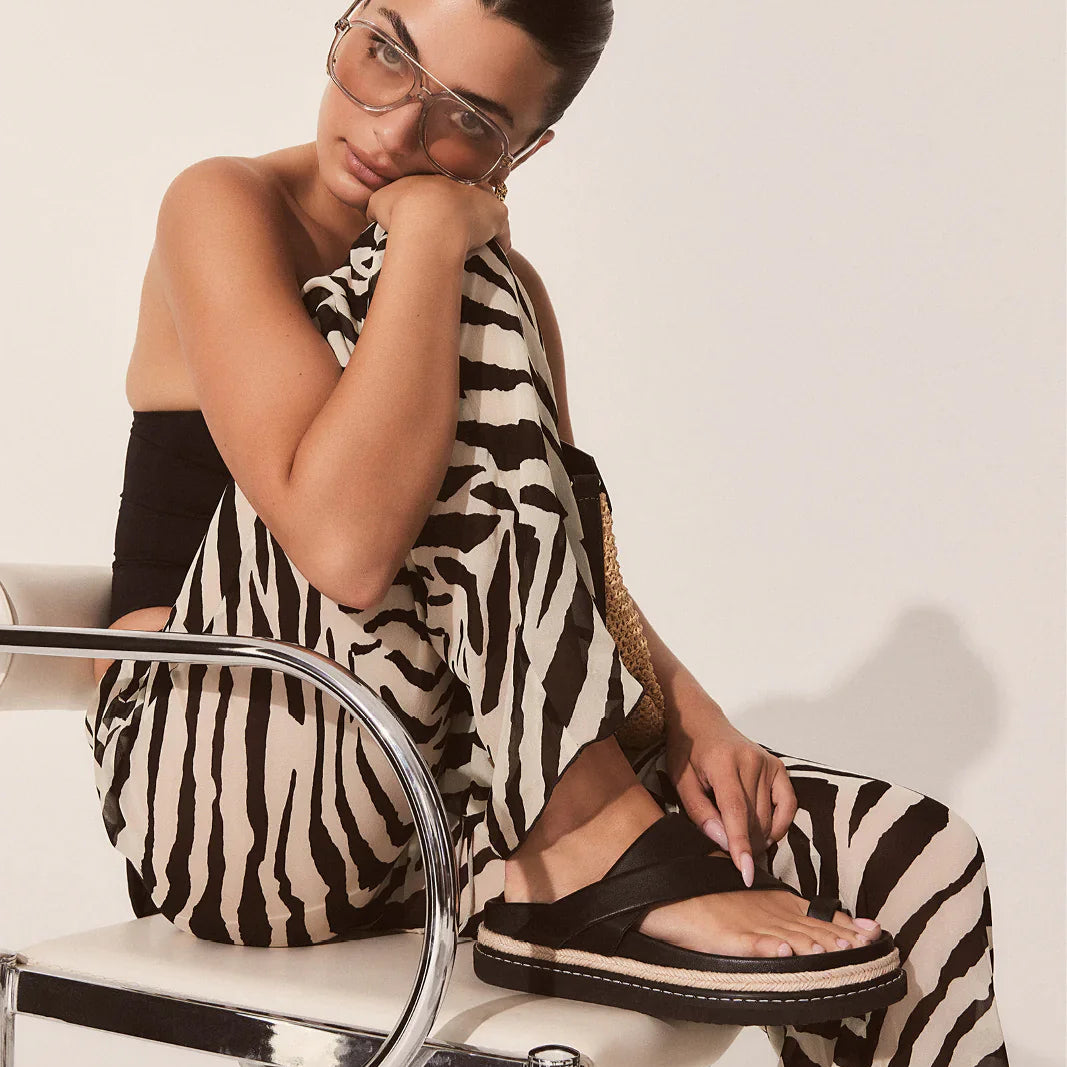 Woman wearing a zebra print outfit sitting on a chair with a plain background